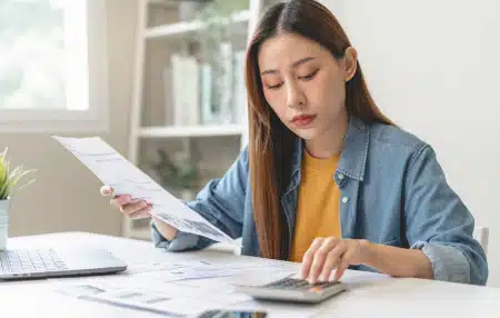 woman holding piece of paper and tapping on calculator