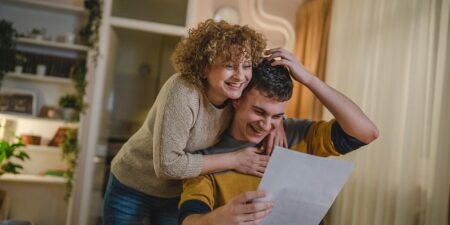 Woman hugging man reading letter and smiling