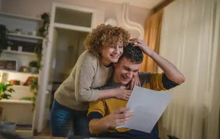 Woman hugging man reading letter and smiling