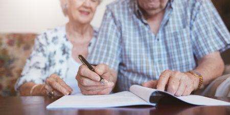 An elderly couple writing in a booklet