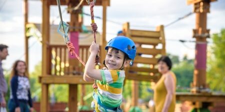 A child on a zipwire at a playground with family in the background