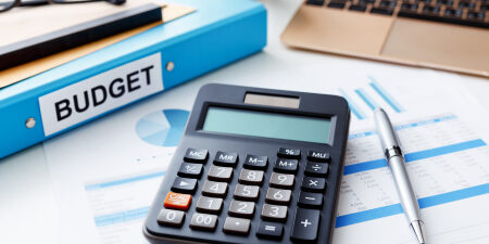 Image of a calculator, pen, laptop, reading glasses and a blue folder titled "budget."