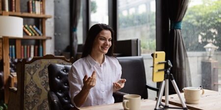 An image of a woman sitting at her desk filming content for social media.
