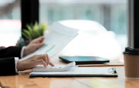 An image of someone typing on their calculator at their desk whilst holding a piece of paper