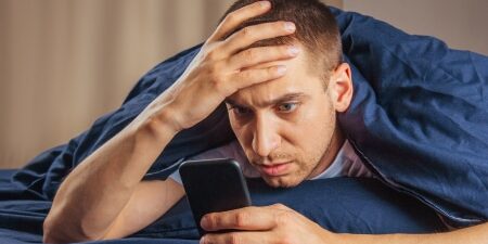 Image of a man lying down in bed on his mobile, looking concerned