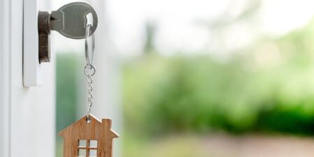 Image of a key in a front door with a wooden house keychain attached