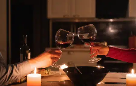 Image of a couple clinking their wine glasses together filled with red wine over a candlelit dinner