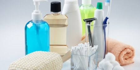 An image of toiletries including an orange flannel, blue bottle of liquid soap, mouthwash, shower gel, toothpaste, cotton ear buds, razors and toothpaste.
