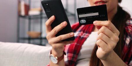 Image of a woman sitting on her sofa with her credit card in one hand and her phone in the other.