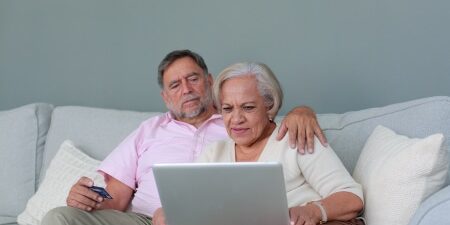 Image of a woman and a man sitting on the sofa looking at their laptop.