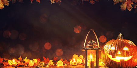 Image of a pumpkin lit up and a lantern on a dark background with autumn leaves