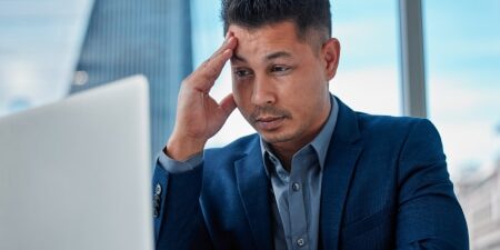 Image of a man with his head in his hands looking at his laptop screen