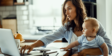Imagine of a woman on her laptop whilst holding her baby