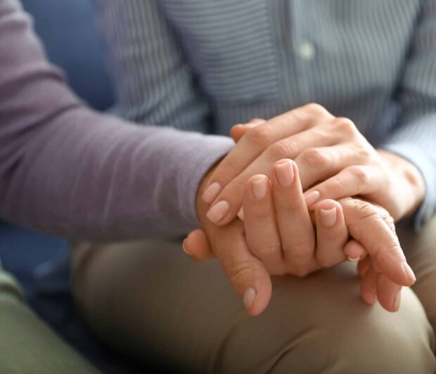 a close up of a young woman’s hand holding the hand of an elderly person.