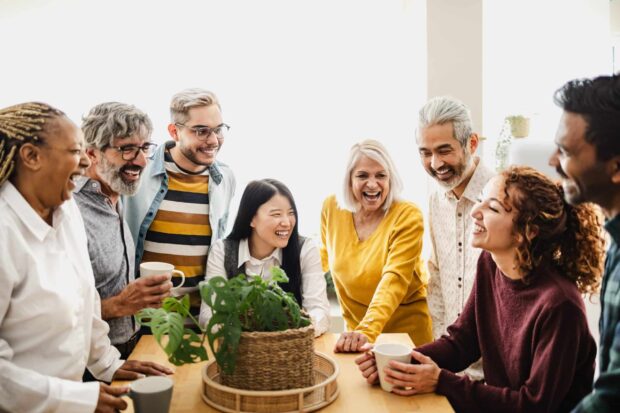 Group of diverse people smiling and talking around a table indoors.