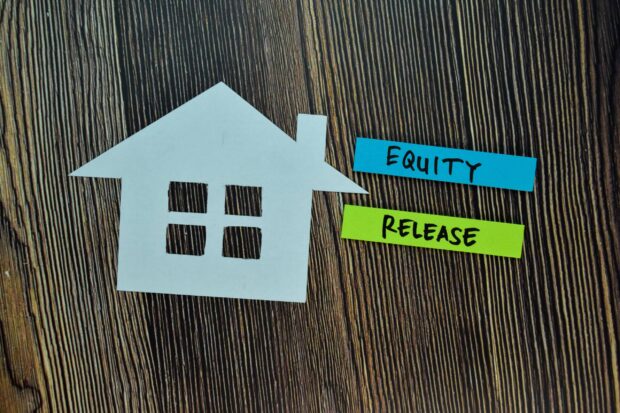 A paper house cutout next to labels reading "Equity" and "Release" on a wooden background.