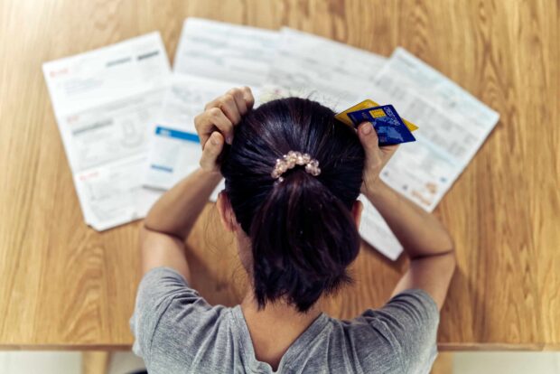Woman holding credit cards, stressed over bills on a table.