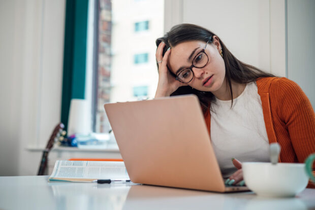 woman-computer Front view of a young woman wearing casual clothing sitting at a desk using a laptop to study, she is a university student. She is feeling stressed and she has her head in her hand.